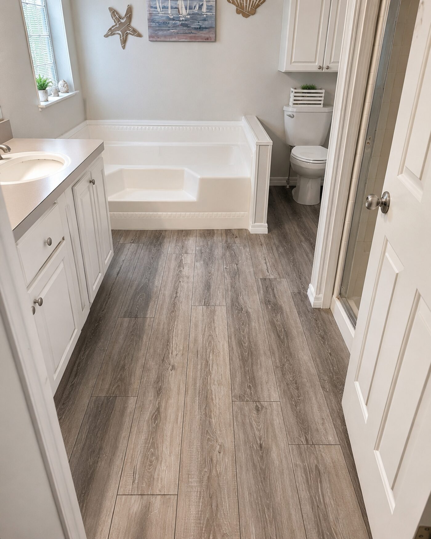 Luxury vinyl plank flooring running through a master bathroom with a soaker tub and vanity